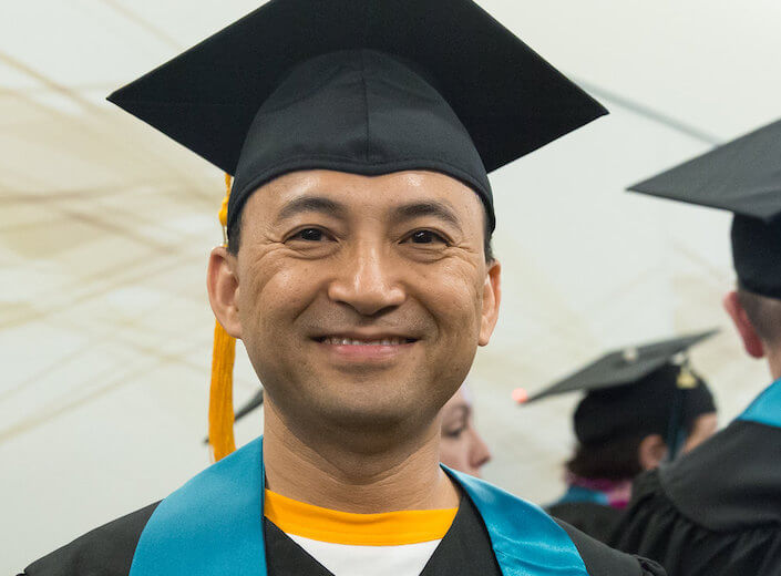 Middle-aged man of Filipino descent wears a cap and gown at a graduation ceremony.