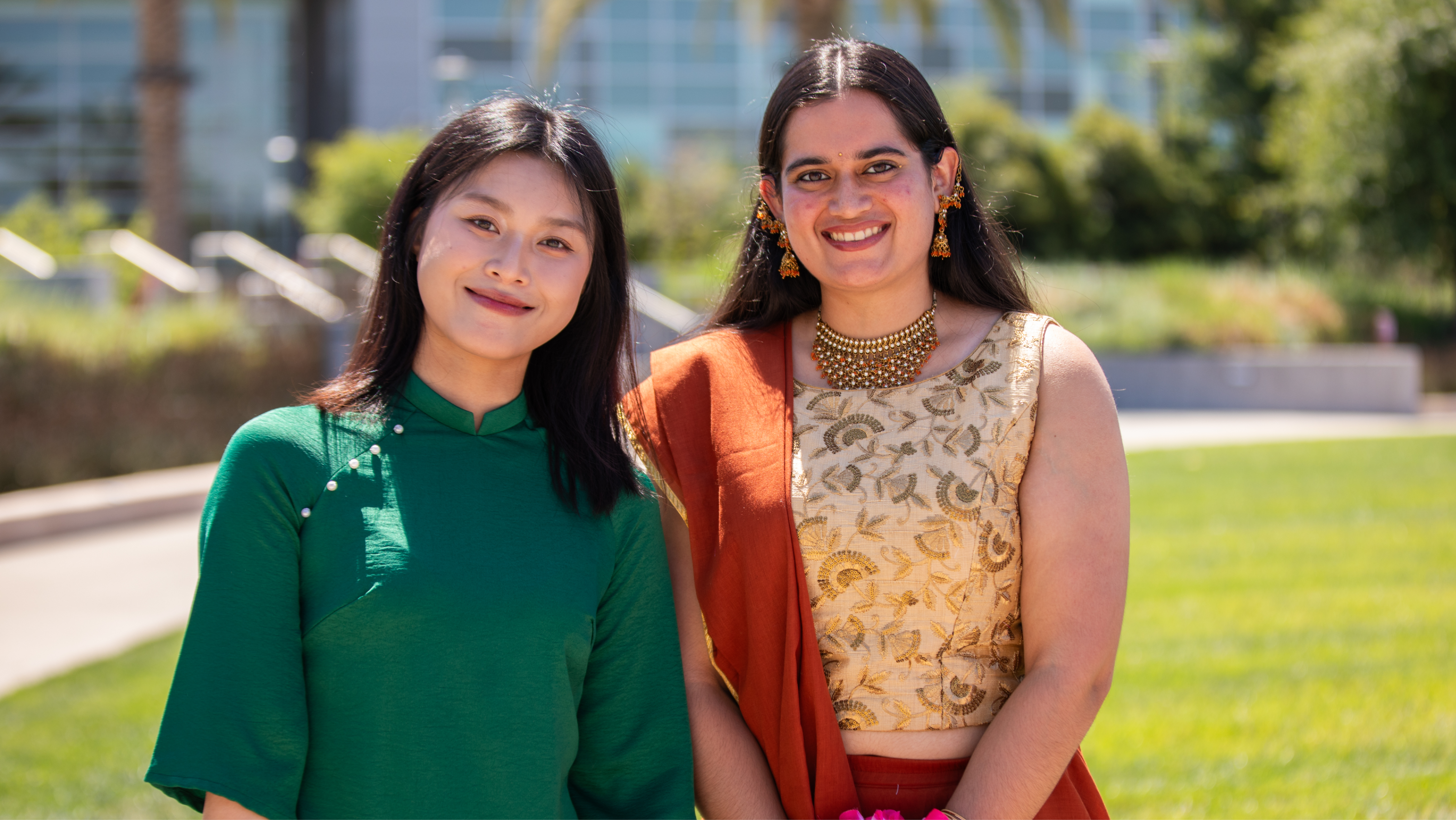 Two women smiling together outdoors on a sunny campus lawn.